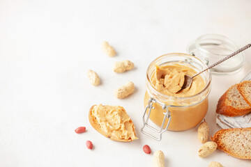 Fototapeta na wymiar Peanut butter or paste jar and heap of nuts on light background.