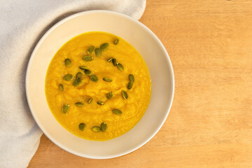 Pumpkin puree soup in a white plate with pumpkin seeds and croutons close-up. Vegetable autumn dish for Halloween or Thanksgiving.