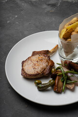 Meat on the bone loin on a white plate with a side dish of potatoes
