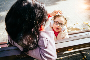 Unrecognizable brunette mother caressing her daughter in headphones outdoor. Family happy moments concept.