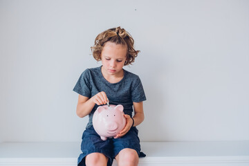 Cute child boy puts coins in a piggy bank as savings. financial education