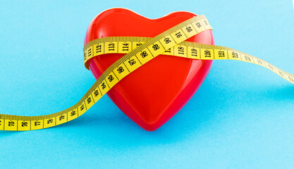 Yellow measuring tape around red heart on blue background