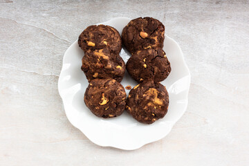 Chocolate cookies cashew nuts raisin in plate on white wood table.
