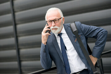 Senior businessman talking on the smart phone in front of corporate office building