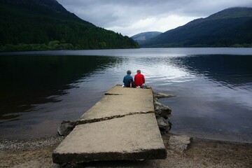 Couple sitting backward looking toward the Loch Lochy freshwater loch and the mountains in Scotland