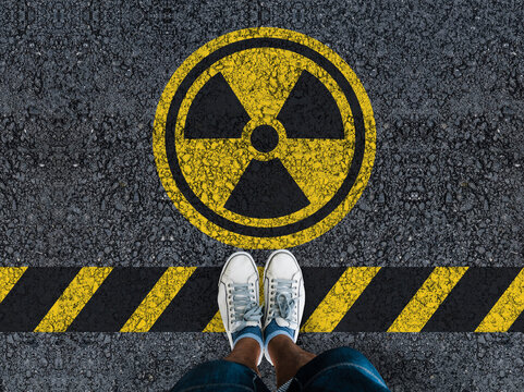 man legs in sneakers standing on asphalt road and radioactive sign
