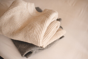 Stack of knitted wool textile sweaters clothes on white blanket in bed at home room close up. Winter cozy season.