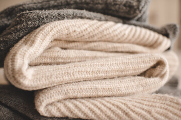 Stack of knitted wool textile sweaters clothes on white blanket in bed at home room close up. Winter cozy season.