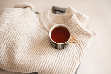 Cup of coffee stay on stack of knitted textile sweater in bed close up top view. Winter cozy season.