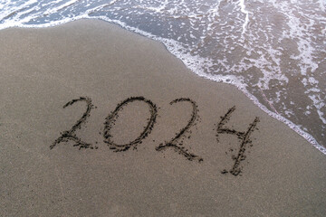 Text Happy New Year 2024 on a sandy sea beach with a small wave. Abstract background photo of the upcoming New Year 2023