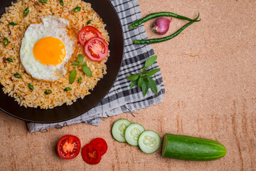 Fried rice served with fried eggs, sliced ​​tomatoes, green chilies, cucumber and onions in a...