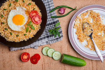 Fried rice served with fried egg, sliced ​​tomato, green chili, cucumber and onion in a skillet and plate. on a wooden background. top view.