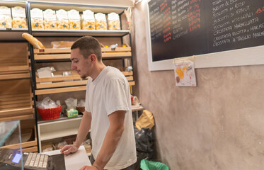Young baker at the cash register making a receipt for a customer