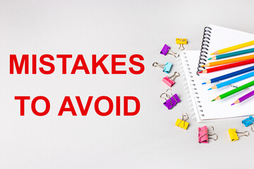 Notebooks, colored pencils and paper clips on a light gray table. The inscription MISTAKES TO AVOID. Banner