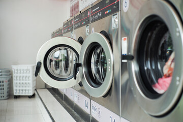 Selective focus on the front door of the washing machine with blurred close doors in foreground. Row of washers in the washing shop