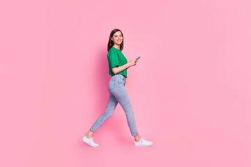 Fototapeta na wymiar Full size profile photo of cheerful nice girl hold use telephone walking isolated on pink color background