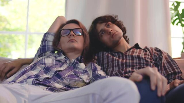 Loving Same Sex Male Couple Lying On Sofa At Home Watching Tv And Relaxing. Realtime