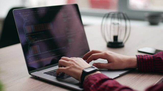 Close up of freelancer's hands typing code on laptop keyboard. Camera slides around developer's figers writing program code on computer display. Programmer working on online application database.