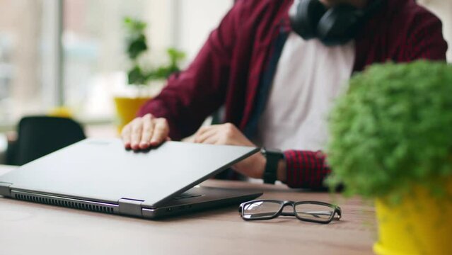 Tired office worker finishes work, takes a break, closes laptop. Overworked developer ends working day in coworking, goes home. Freelancer ends project, leaves workplace with eyeglasses for lunch.
