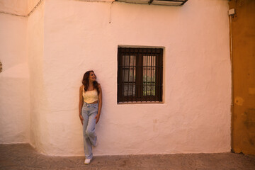 Obraz na płótnie Canvas Young beautiful woman dressed in casual clothes leaning against a white wall of an old house in seville. The woman is making different expressions and postures and is enjoying her holidays.