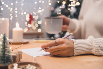 Goals plans make to do and wish list for new year christmas concept, girl writing in notebook. Woman hand holding pen on notepad at home on winter holidays xmas. Christmas decoration, gift boxes. 