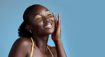 Yellow makeup and black woman face beauty for skincare cosmetic product with blue studio wall. Thinking, contemplating and pensive African girl feeling soft skin texture with eyeshadow mockup. - obrazy, fototapety, plakaty