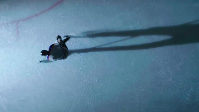 Cinematic view of skilled ice hockey player practicing alone, under a single light which causes a long, dramatic shadow
