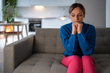 Young woman wearing blue sweater thinks about recent breaking up with boyfriend. Female freelancer...