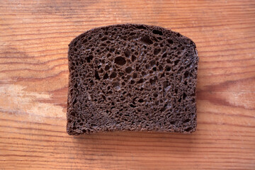 A piece of black rye bread lies on an old wooden board. Food crisis concept