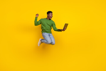 Full length body size view of handsome trendy guy jumping using laptop rejoicing isolated over vivid yellow color background