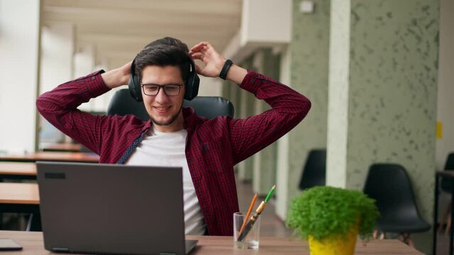 Developer, video editor man in headphones working with laptop at spacious coworking alone enjoying music. Stylish creative musician producer listens song in office alone. Online gamer playing games.