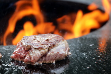 Steak while preparing with flames in soft focus in background