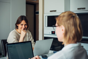 Coworking, remote work, home office, startup. Two young pretty women sitting with laptops facing each other, focus on the brunette's face.