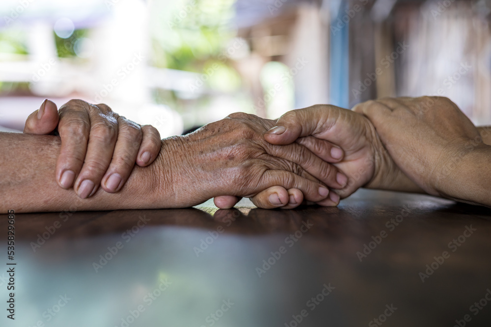 Wall mural low angle close-up shot of two wrinkled hands of two elderly thai women holding each other in consol