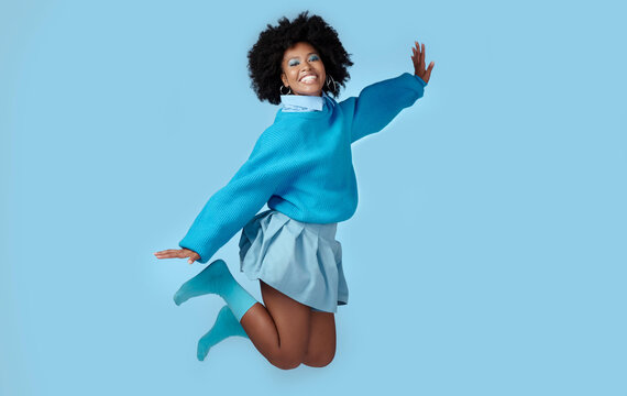 Blue, jump and happy black woman in a studio with trendy, cool and stylish clothes with a background. Happiness, smile and portrait of a young african model with energy, excited and joy.