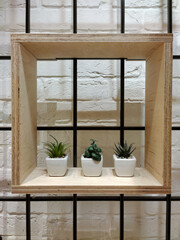 A decorative wooden square shelf with three flower pots hangs on a brick wall