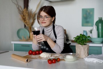A caring wife prepares dinner with a glass of wine. Relaxation with alcohol in the kitchen.