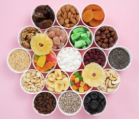 Nuts, seeds, dried fruits in round containers. Background with a mix of healthy snacks. Assorted vitamin food on a pink background.