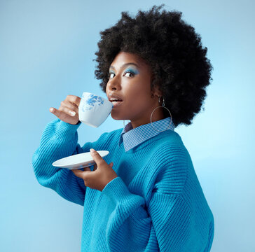 Afro hair, tea cup and black woman with fashion, style and trend clothes on blue background in studio with bold makeup cosmetics. Portrait, gossip and beauty model with wow or surprise face and drink
