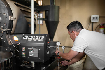 An Hispanic man is setting the buttons to turn on the coffee roaster machine