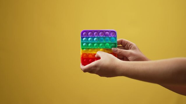Female Caucasian hand playing multicolored fidget toy in slow motion at yellow background. Unrecognizable young woman showing sensory toy advertising stress relief