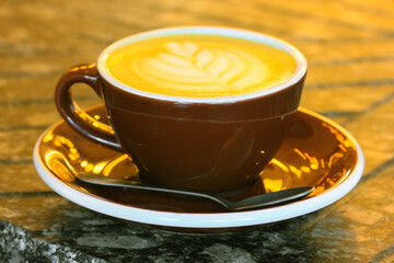 Brown ceramic cappuccino cup, freshly brewed coffee with milk on a wooden table. Beautifully decorated caffeine drink. Serving a warm autumnal season beverage in cafe, restaurant. Latte art concept.