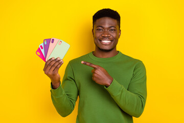Portrait of handsome trendy cheerful guy holidng demonstrating mobile cases isolated on bright yellow color background