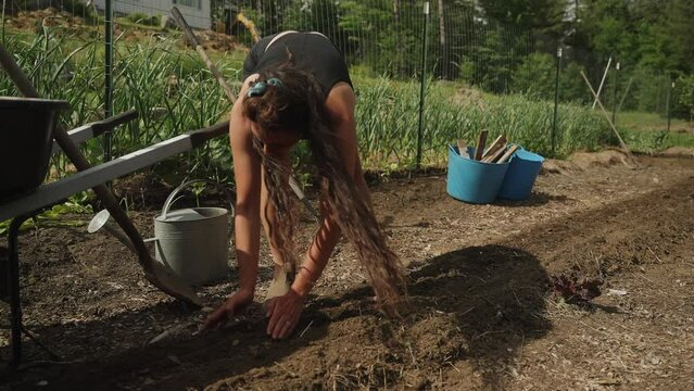 Girl with long hair planting seeds in farm garden working (4k 30p Slow Motion)