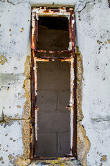 Derelict metal window frame set into a delapidated block wall