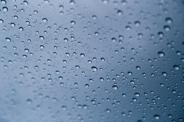 Close up of rain drops on window with blue gray background of dark sky.