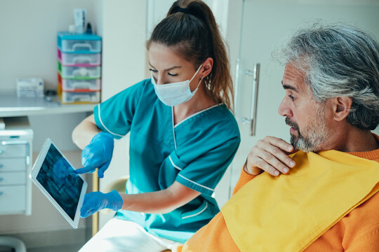 Dentist talking to worried male patient and showing a digital tablet with x-ray film in a dental clinic