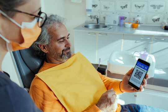 Smiling Male Patient Showing Vaccine Passport on his Mobile Phone App at Dentist's Office