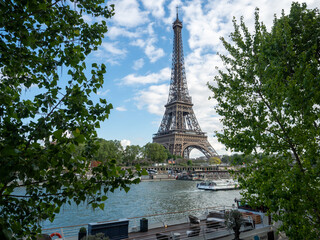 Fototapeta na wymiar Eiffel tower across Seine River through trees as boat passes