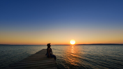 Traveler asian woman with her summer vacations on a twilight by the sea her sitting on bridge lonely dramatic lifestyle. Aegean Sea Beach, Canakkale, Turkye. Leave a blank and space for text entry.